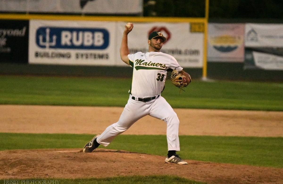 Baseball pitcher in white uniform mid-throw on the mound during a night game